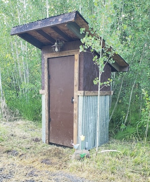 Een kleine houten schuur met een golfplaten deur en een schuin dak.