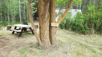 Una mesa de picnic con banco y un cartel en un árbol en una zona boscosa.