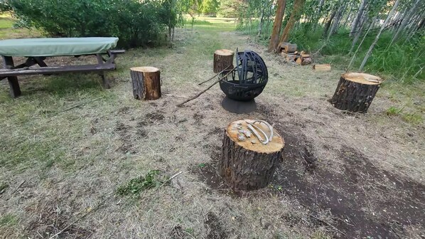 A picnic area with a table and benches, surrounded by stumps and a black spherical object.