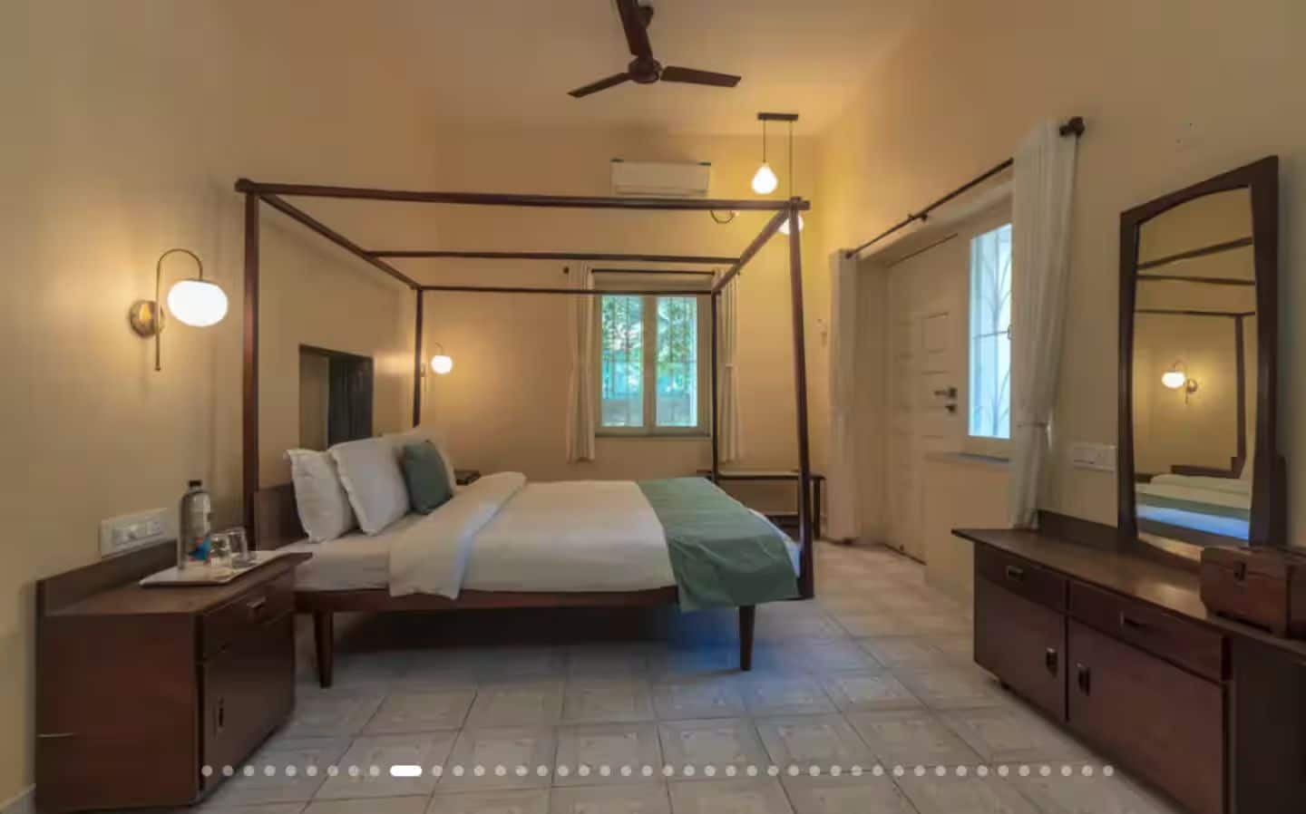 A four-poster bed with a canopy, a bedside table with a lamp, a large mirror, and a window with curtains.