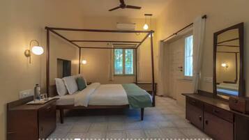 A four-poster bed with a canopy, a bedside table with a lamp, a large mirror, and a window with curtains.