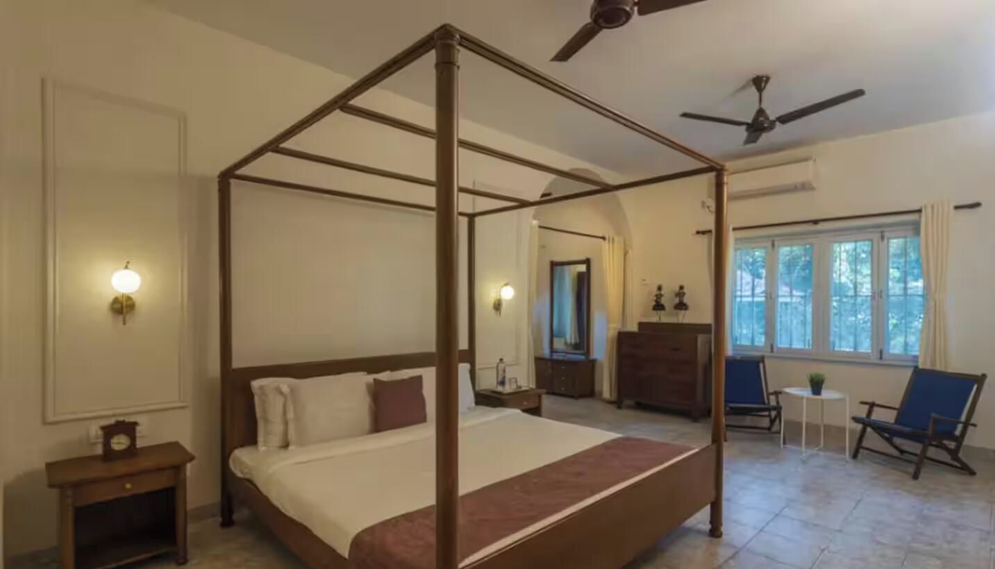 A four-poster bed with a wooden frame, a ceiling fan, and a view of the outdoors through a window.