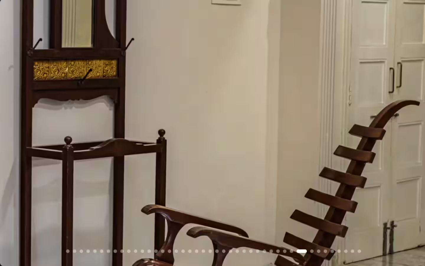 A wooden chair with a curved backrest and a metal frame, positioned in a hallway with white walls and a door in the background.