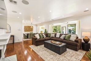 A modern living room with a sectional sofa, a coffee table, and a dining area with chairs. - The Sherwood Serenity in the City (Los Angeles)