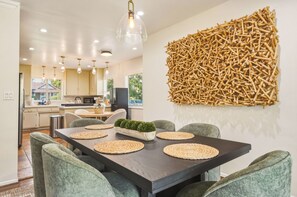 A modern dining area with a dark wooden table, woven placemats, and green upholstered chairs. - The Sherwood Serenity in the City (Los Angeles)