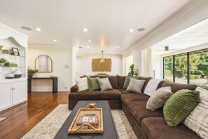 A modern living room with a sectional sofa, a coffee table, and a large window providing a view of the outdoors. - The Sherwood Serenity in the City (Los Angeles)
