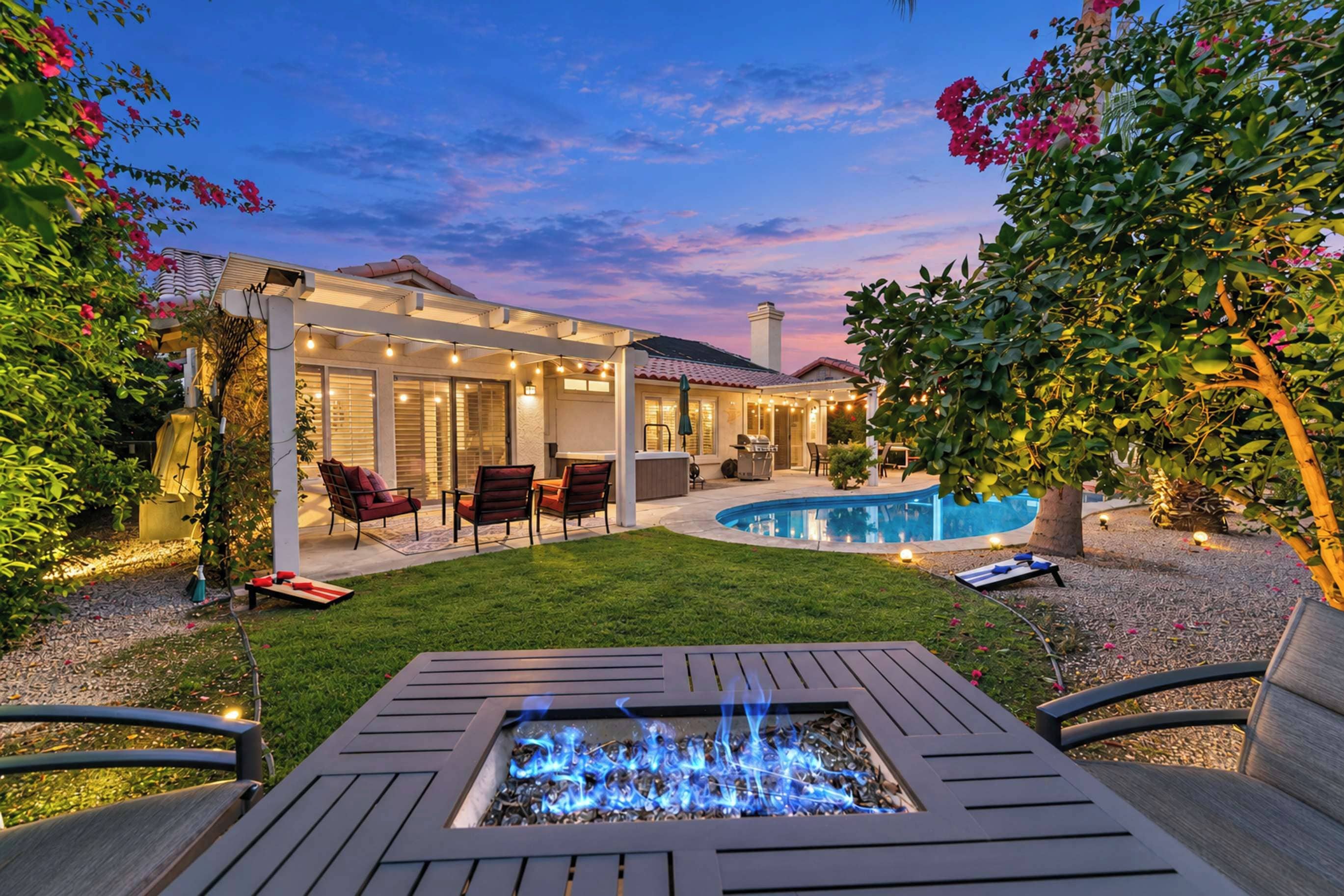 A backyard with a fire pit, outdoor seating, a swimming pool, and a covered patio area.