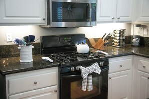 A kitchen with a stainless steel microwave, a gas stove, a kettle, and various kitchen utensils. - Private Pool, Spa & Game Room 4BR La Quinta (La Quinta)