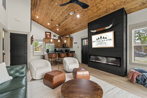 A modern living room with a fireplace, leather furniture, and a kitchen in the background. - Bungalow Bliss | NEW | Swim Spa 💦 Private Fire Pit 🔥 (Hollister)