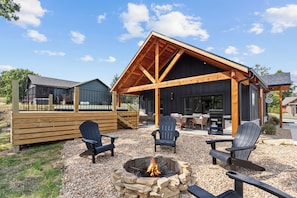 A wooden deck with Adirondack chairs, a stone fire pit, and a covered outdoor seating area with a grill. - Bungalow Bliss | NEW | Swim Spa 💦 Private Fire Pit 🔥 (Hollister)