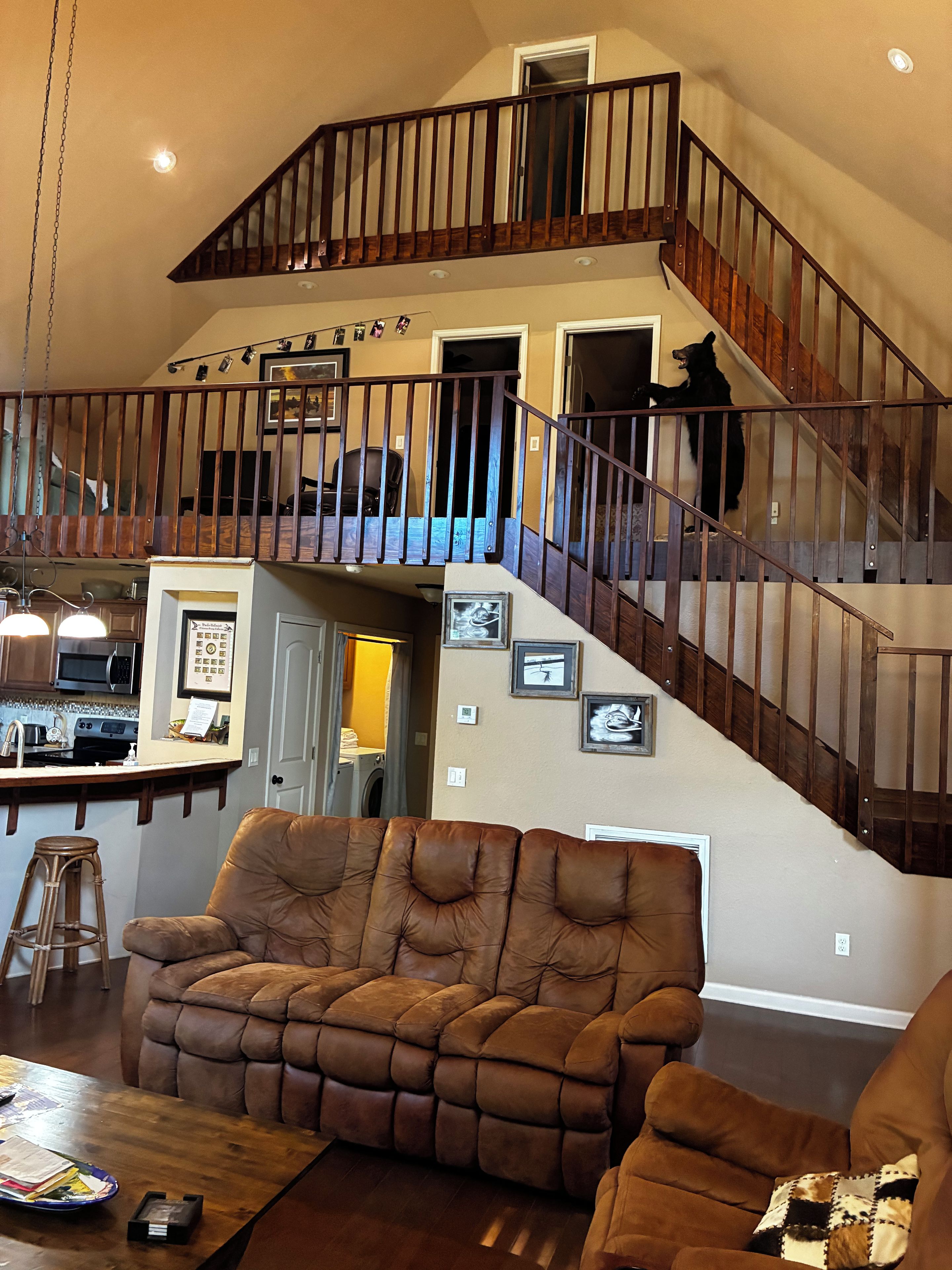 A spacious living area with a brown leather sofa, a wooden coffee table, and a kitchen area with a microwave and sink.