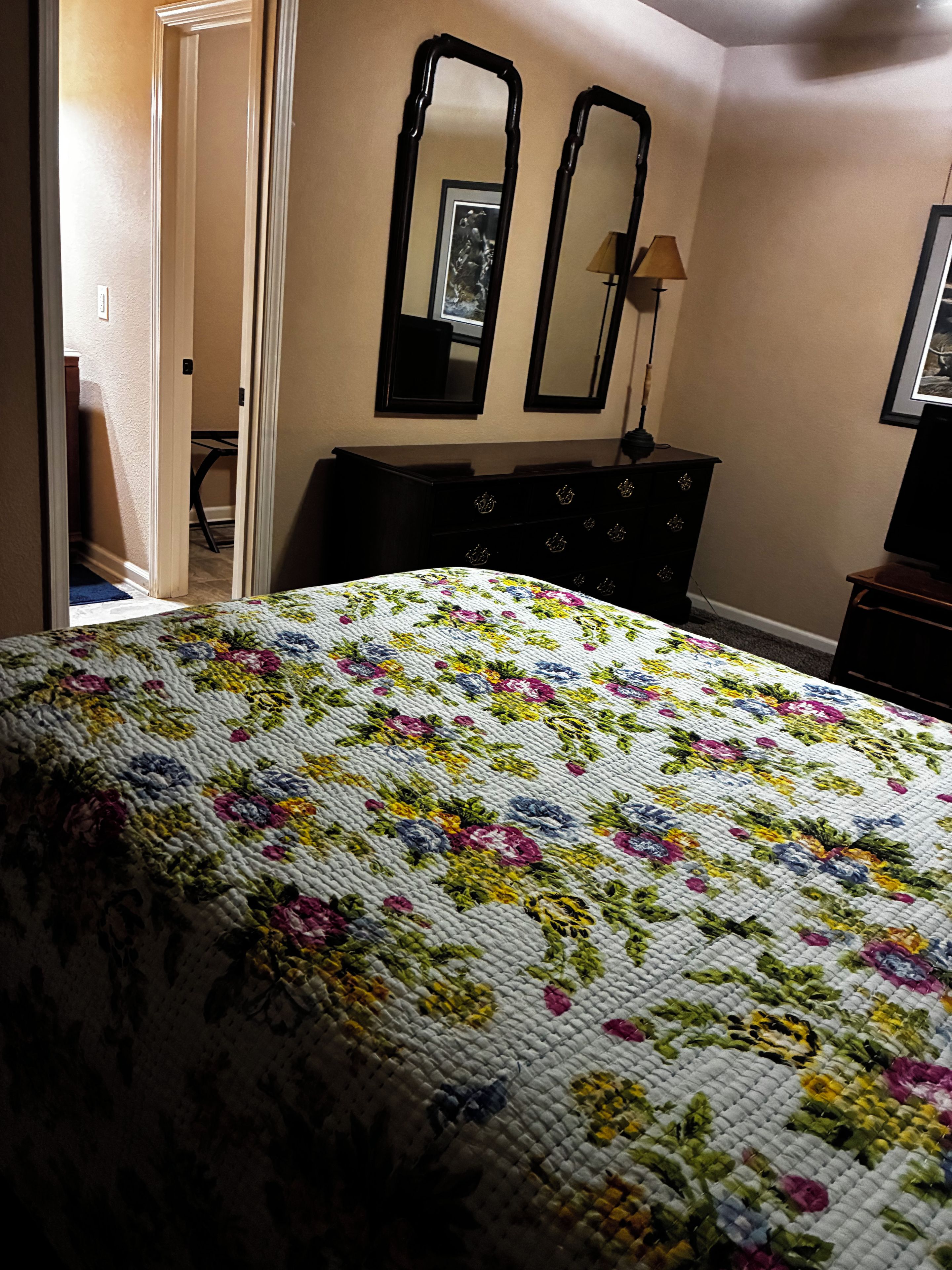 A bedroom with a bed, a dresser, two mirrors, and a lamp.