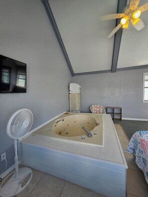 Ein Zimmer mit einer großen Badewanne, einem Deckenventilator, einem Spiegel und einem Fenster.