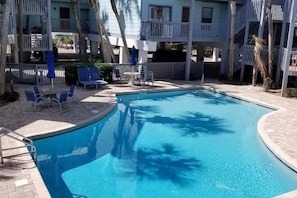 A swimming pool with a curved edge, surrounded by lounge chairs and a small table. - Ocean Reef 901 Family Friendly 3-bedroom Townhome (Gulf Shores)