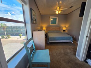 A hotel room with a bed, a desk, a chair, a ceiling fan, and a window with a view of the outside. - Ocean Reef 901 Family Friendly 3-bedroom Townhome (Gulf Shores)