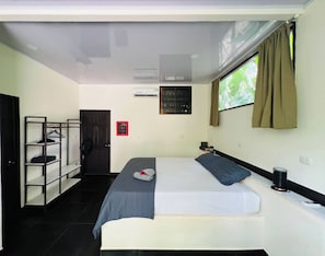 A hotel room with a bed, a shelf unit, a door, and a window with curtains. - Private Jungle Box in Playa Cocles (Cahuita)