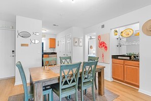 A modern kitchen with wooden cabinets, a dining area with a wooden table and teal chairs, and a kitchen island with a decorative flamingo painting. - Seabrook Exclusives | 2013 Marsh Walk (Seabrook Island)