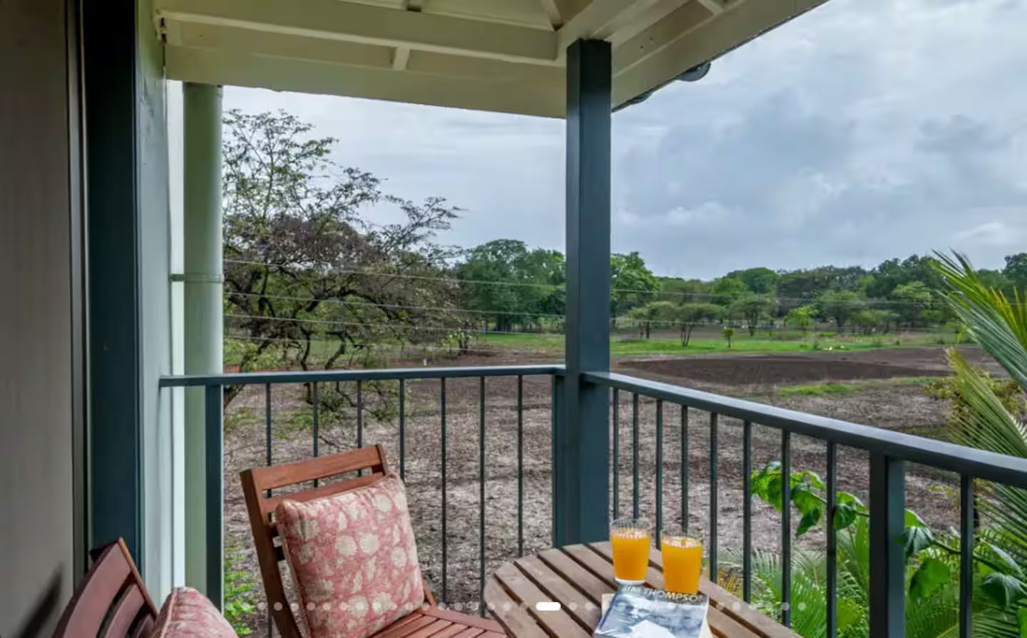 Een balkon met een houten stoel en een tafel, met uitzicht op een groen landschap met bomen en velden.