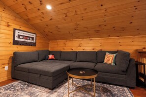 A cozy room with a sectional sofa, a small round table, and a wooden ceiling.