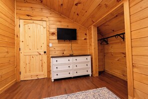 A wooden room with a white dresser, a flat-screen TV mounted on the wall, and a wooden door. - Gorge Getaway | Hot Tub • Near Muir Valley (Rogers)