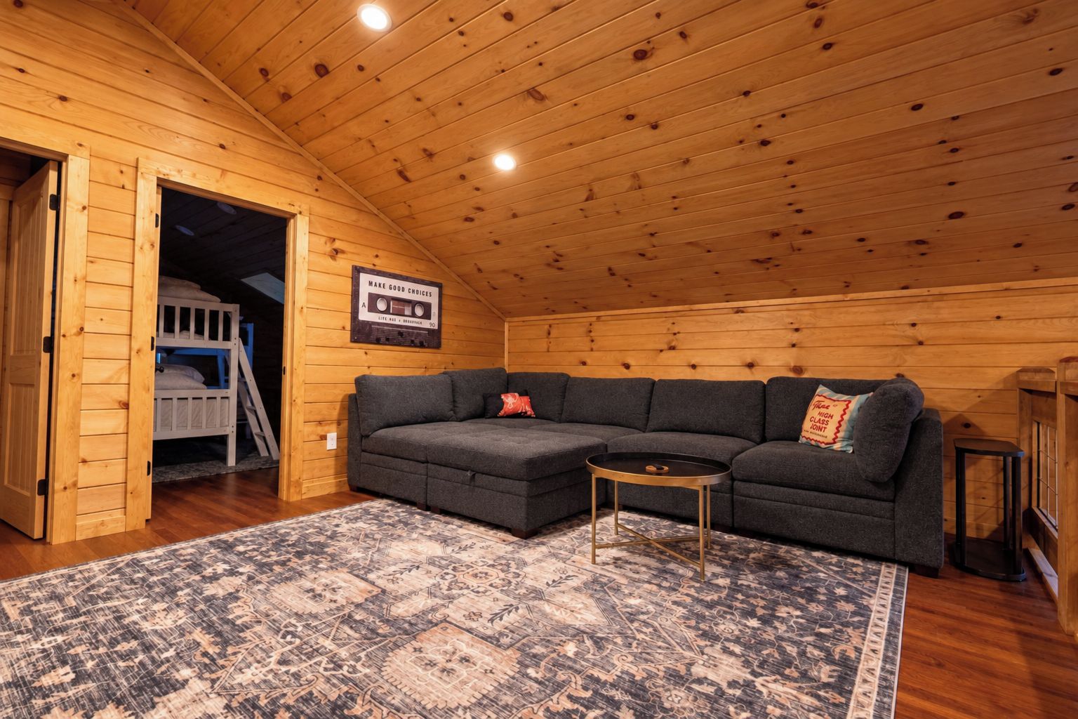 A cozy cabin interior with a gray sectional sofa, a small round table, and a patterned rug.
