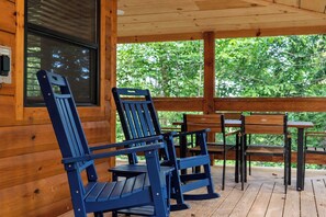 A wooden deck with a table and chairs, a window, and a view of greenery. - Gorge Getaway | Hot Tub • Near Muir Valley (Rogers)