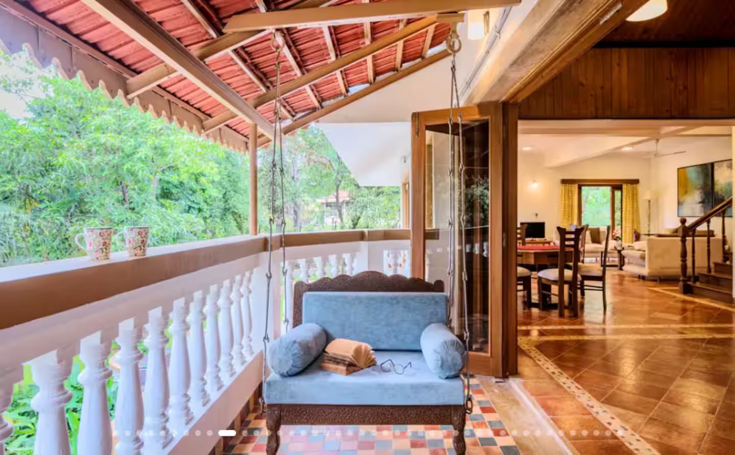 A cozy balcony with a cushioned seating area, a dining area with chairs, and a view of greenery.