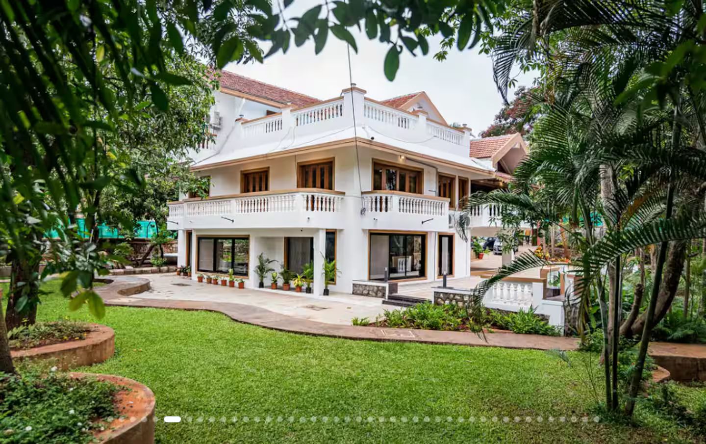 A two-story house with a balcony, surrounded by a well-maintained garden.