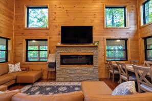 Un intérieur de chalet chaleureux avec une cheminée en pierre, des murs en bois, un téléviseur à écran plat et un coin repas.
