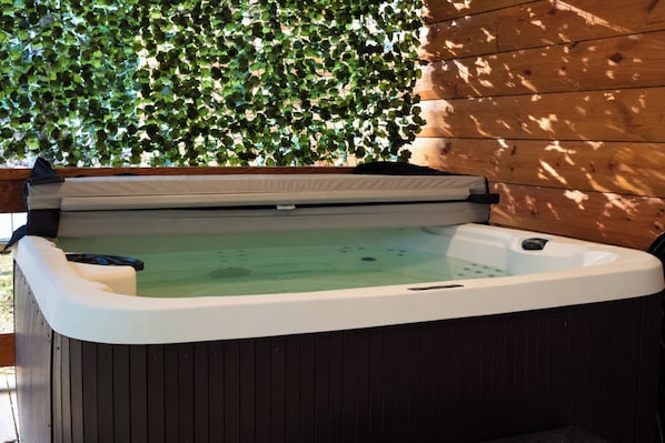 A hot tub with a wooden deck and a green leafy wall in the background. - Gorge Haven | Hot Tub • Near Muir Valley (Rogers)