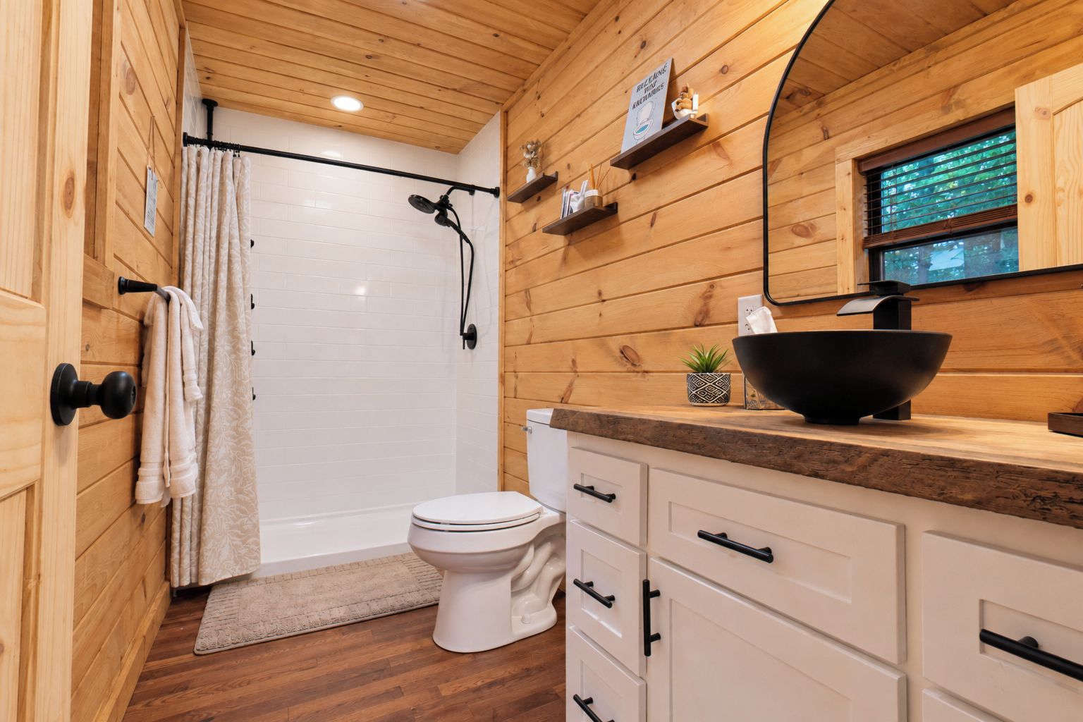 A wooden interior with a white toilet, a shower area, and a sink with a black basin.