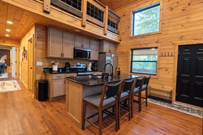 A kitchen with wooden cabinets, a microwave, a stove, and a bar area with chairs.