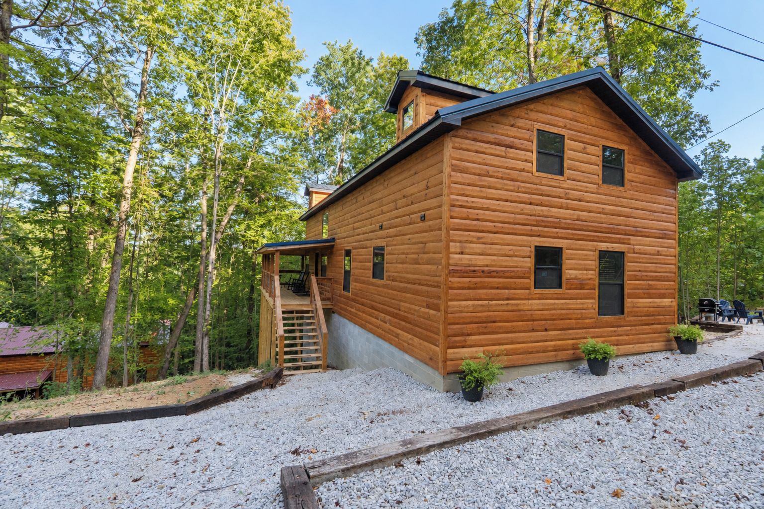 A wooden cabin with a covered porch, a staircase, and a gravel driveway.
