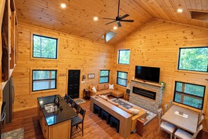 A cabin interior with a kitchen, dining area, and living room, featuring wooden walls and large windows.