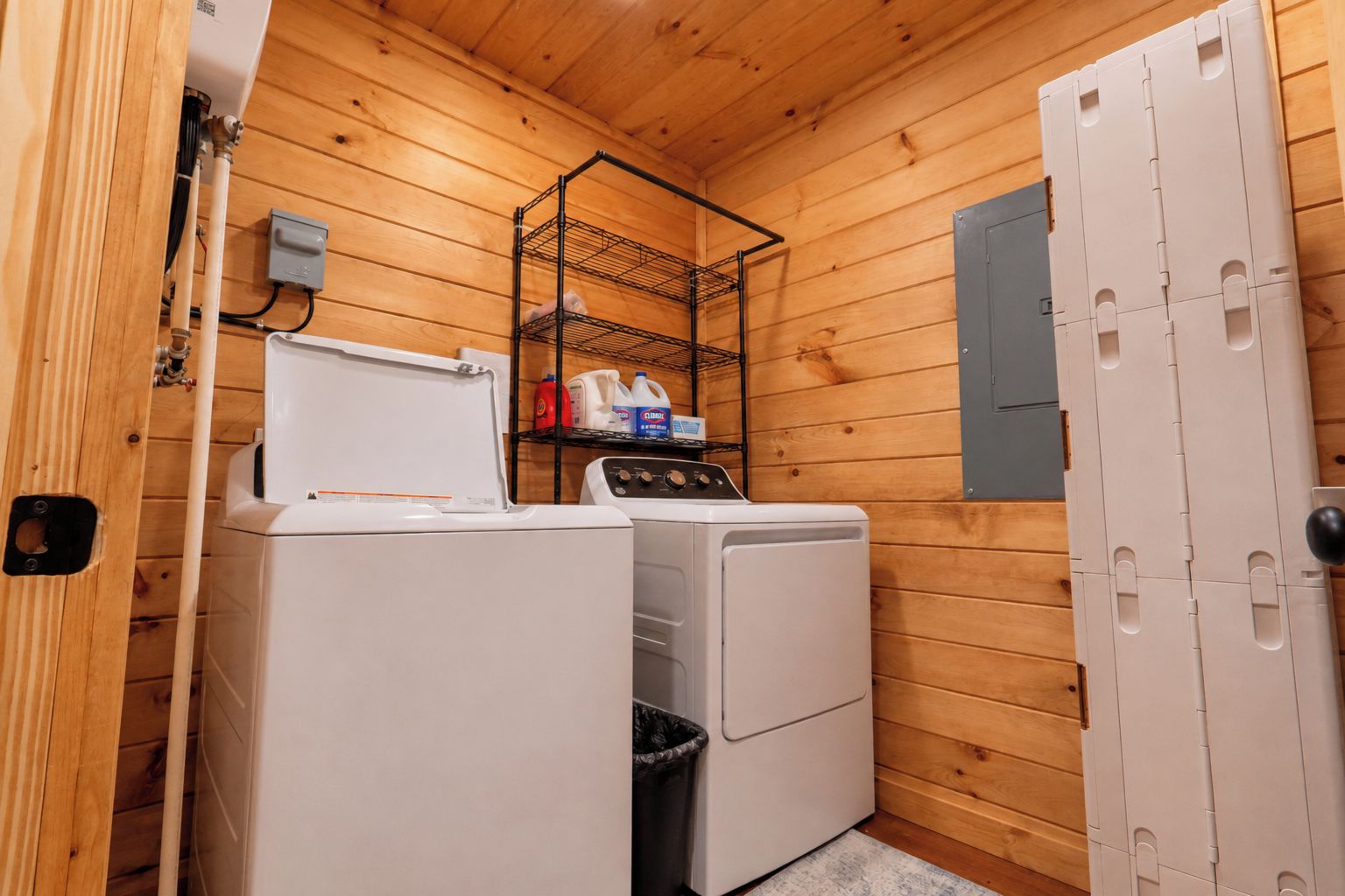 A compact laundry room with a washing machine, dryer, and a metal shelf with detergent bottles.