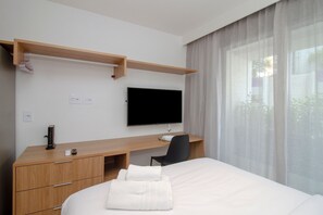 A hotel room with a bed, a desk, a chair, a flat-screen TV, and a window with sheer curtains. - Valen capote valente  (São Paulo)
