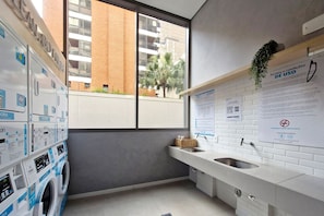 Un moderno lavadero con varias lavadoras, un lavabo y carteles informativos en la pared.