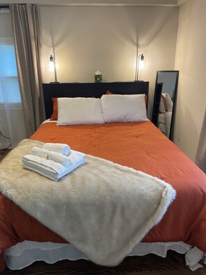 A neatly made bed with an orange bedspread, white pillows, and a fluffy white throw blanket. - Peaceful Homestead: 2BR/2BA + Office & Garden (Decatur)