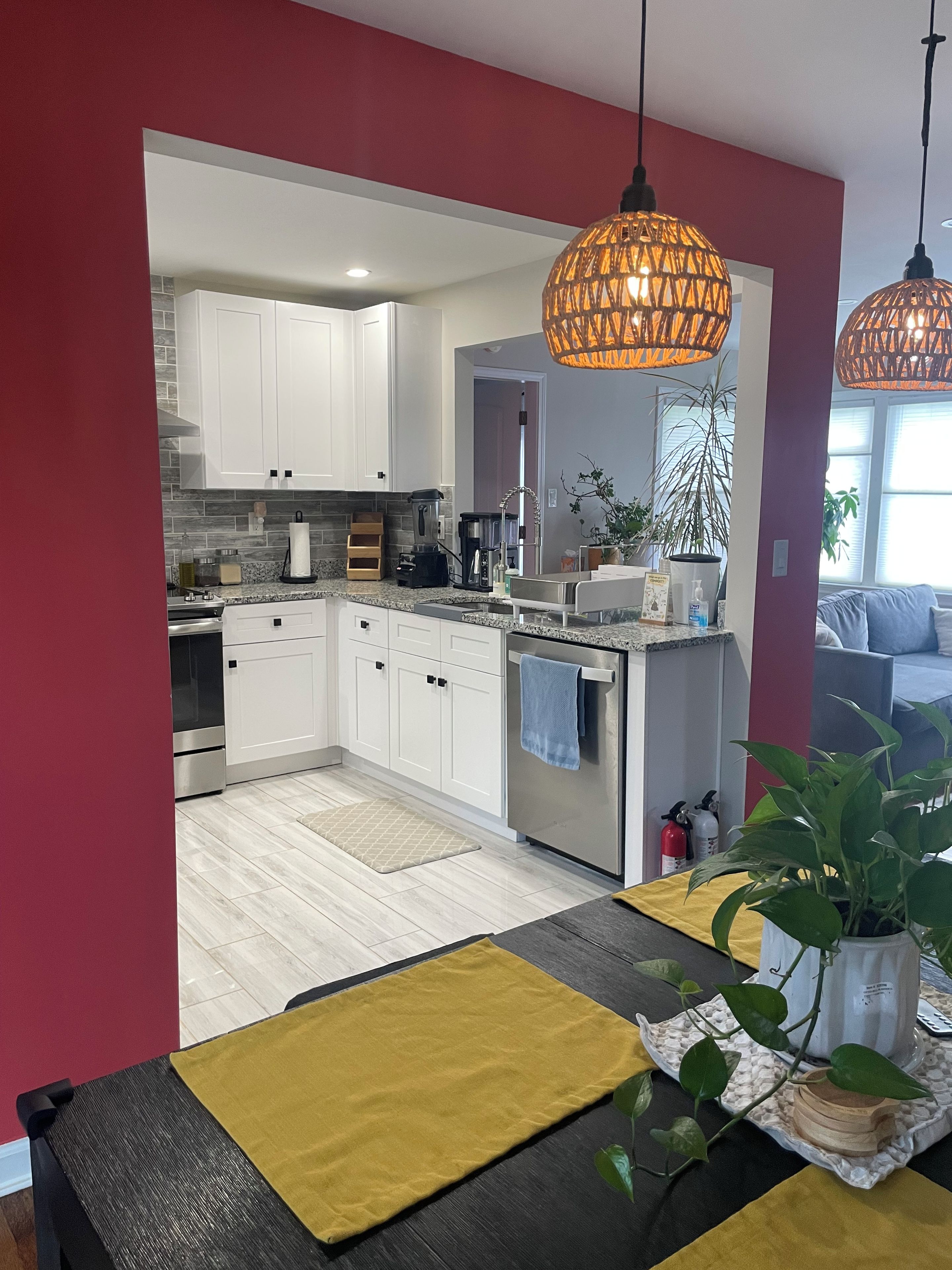 A modern kitchen with white cabinets, a coffee maker, and a sink. There are hanging lights and a plant on the counter.