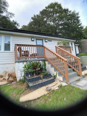 A residential house with a wooden staircase, a front porch with a chair, and a small garden area with plants. - Peaceful Homestead: 2BR/2BA + Office & Garden (Decatur)