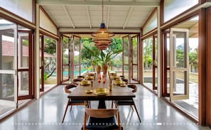 A dining area with a long table, chairs, and a hanging light fixture. - Serene Luxury Villa with Infinity Pool & Garden (Ramanagara)