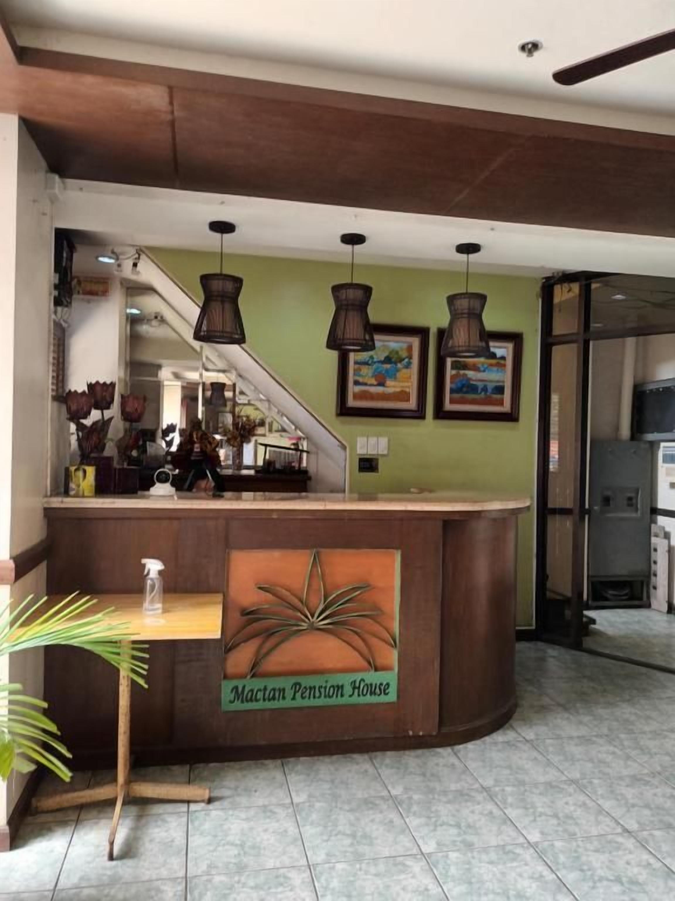 A reception desk with a sign for 'Mactan Pension House,' a staircase, and a view of the interior.
