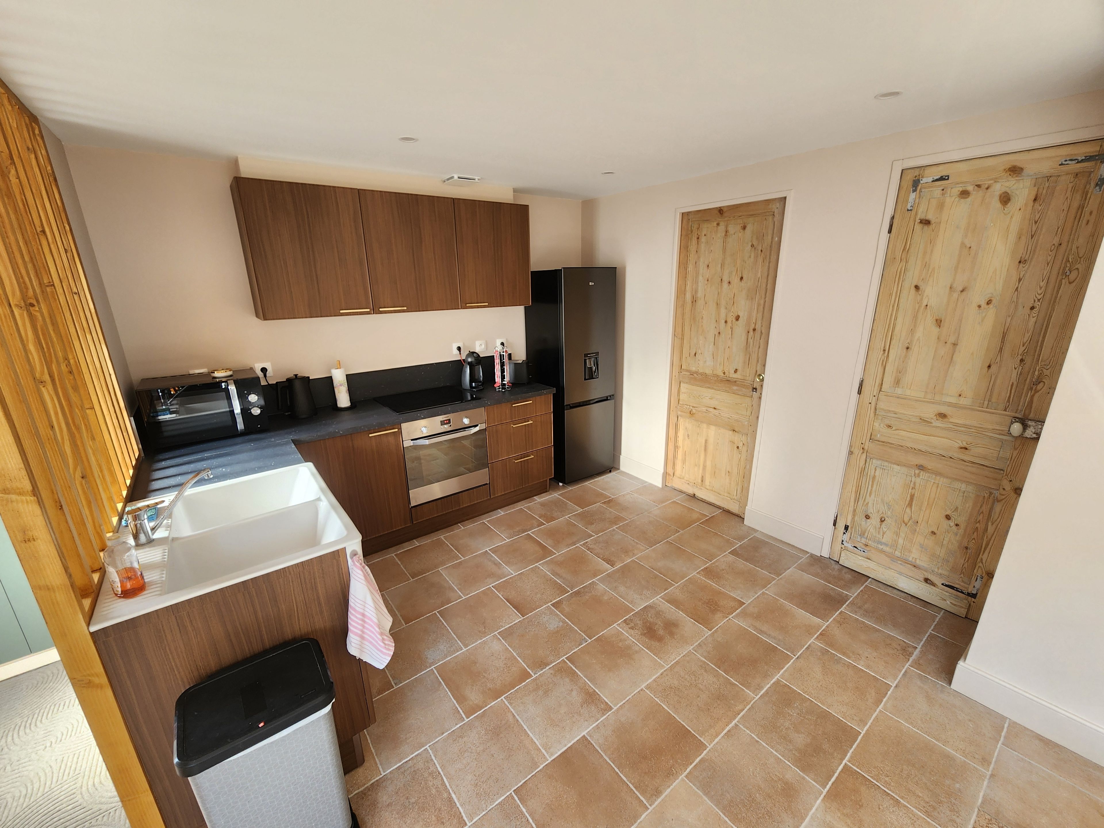 A compact kitchen with wooden cabinets, a stainless steel refrigerator, and a tiled floor.