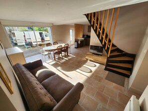Ein Wohnzimmer mit braunem Sofa, einem Esstisch mit Stühlen, einem Fernseher auf einem Holzgestell und einer Treppe mit Holzstufen.