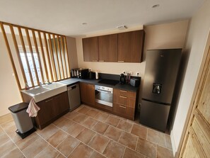 Eine moderne Küche mit Holzausstattung, einem Edelstahlkühlschrank, einer Spülmaschine und einer Arbeitsplatte mit verschiedenen Geräten.