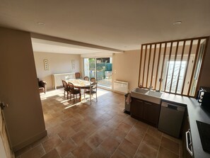 A dining area with a table and chairs, a kitchen with a dishwasher and a sink, and a sliding glass door leading to an outdoor area.