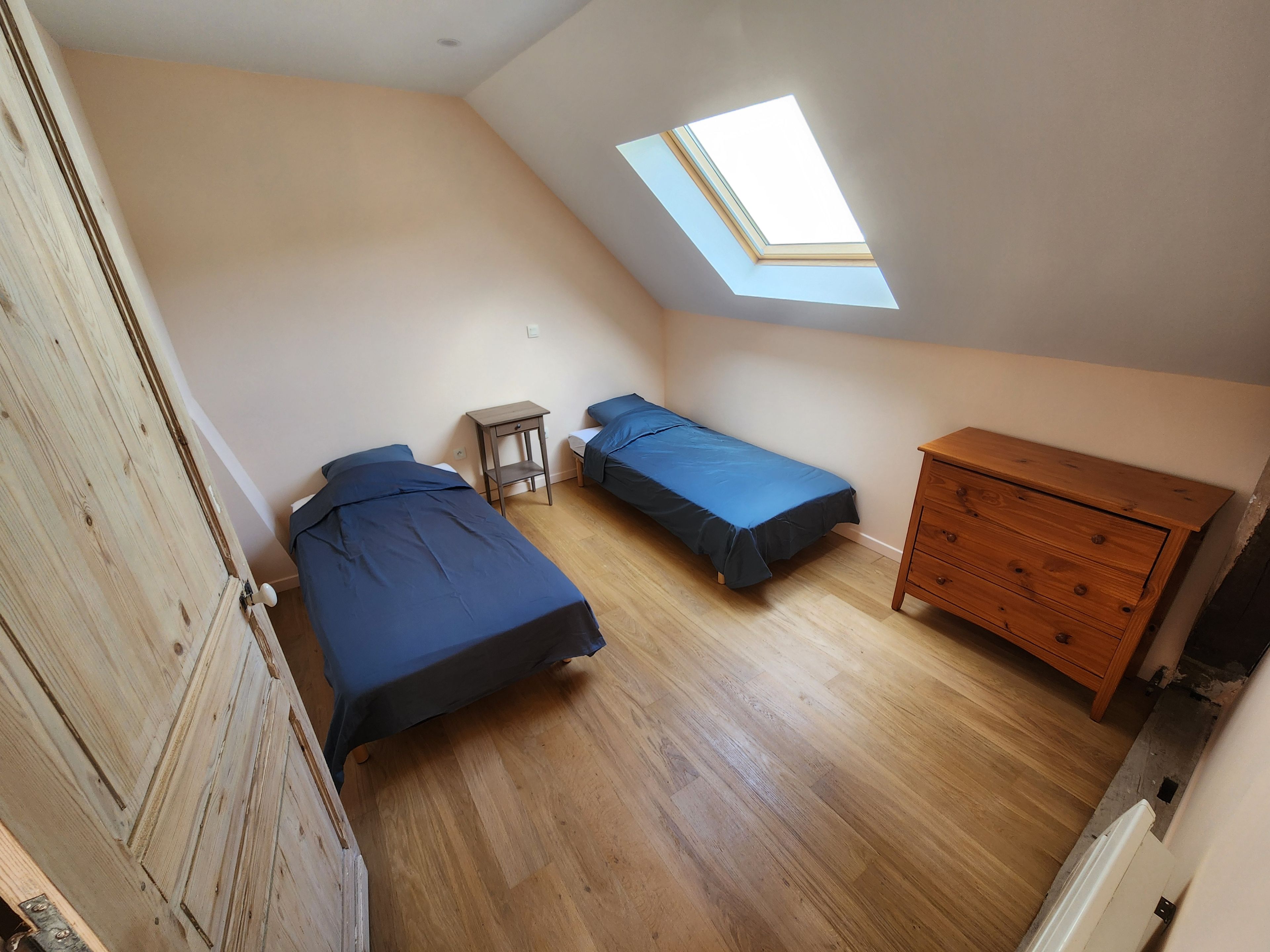 A room with two beds, a wooden dresser, a skylight, and a small table.