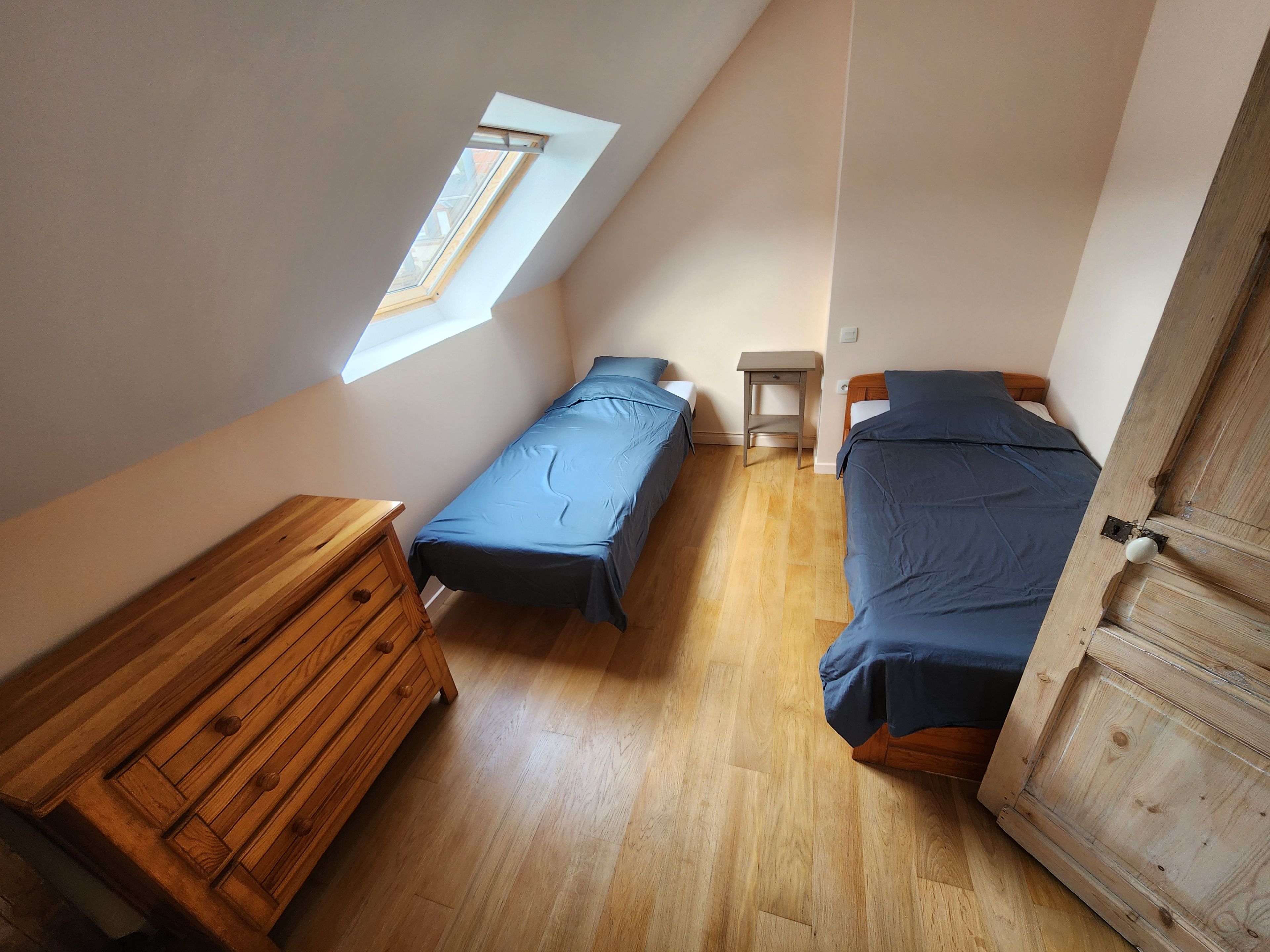 Un petit appartement d’une seule pièce comprenant deux lits, une commode en bois, une petite table et une lucarne.