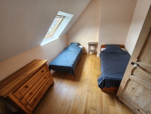 Un apartamento pequeño de una sola habitación con dos camas, un aparador de madera, una mesita y un tragaluz.