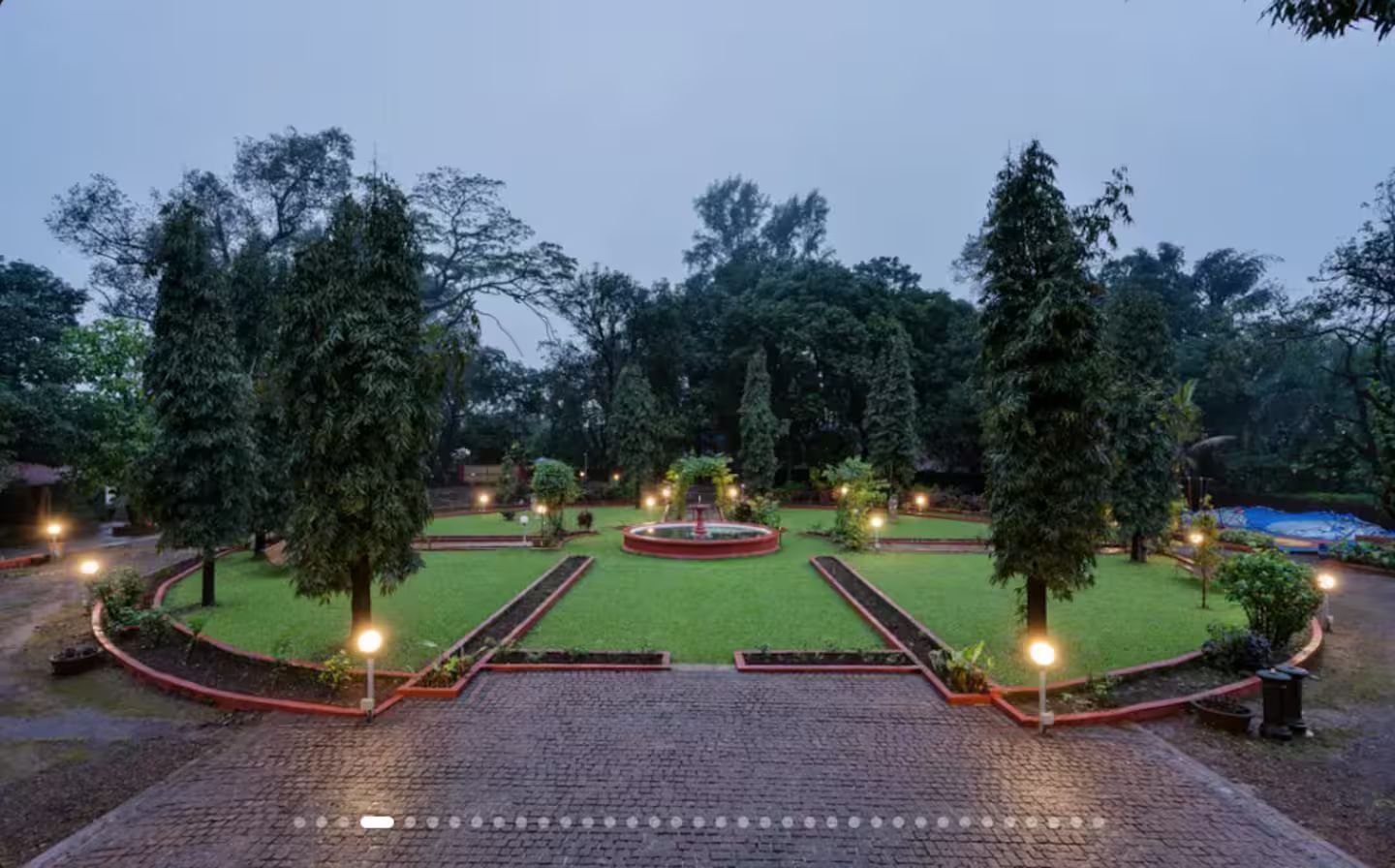 Un jardín ajardinado con una fuente central, rodeado de senderos y árboles.